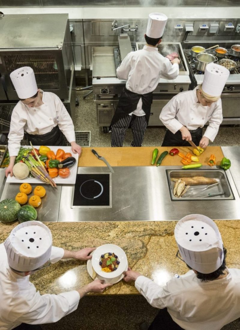 a-view-looking-down-on-a-crew-of-chefs-working-in-a-commercial-kitchen--e1664474298227-pvhjvxvrafkepem0mmuz3go8ni7aagqjoq2xtbcu7s