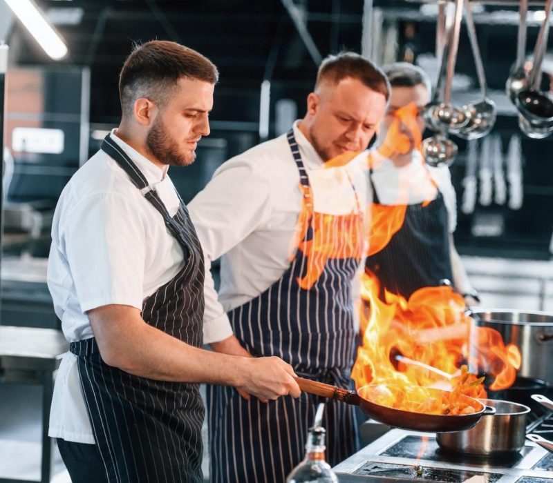 flaming-the-meal-on-frying-pan-kitchen-workers-is-together-preparing-the-food-e1664474312692-pvhjwb1hy405dkpr5htwxy0nfilm6oa20l8efcpfmg